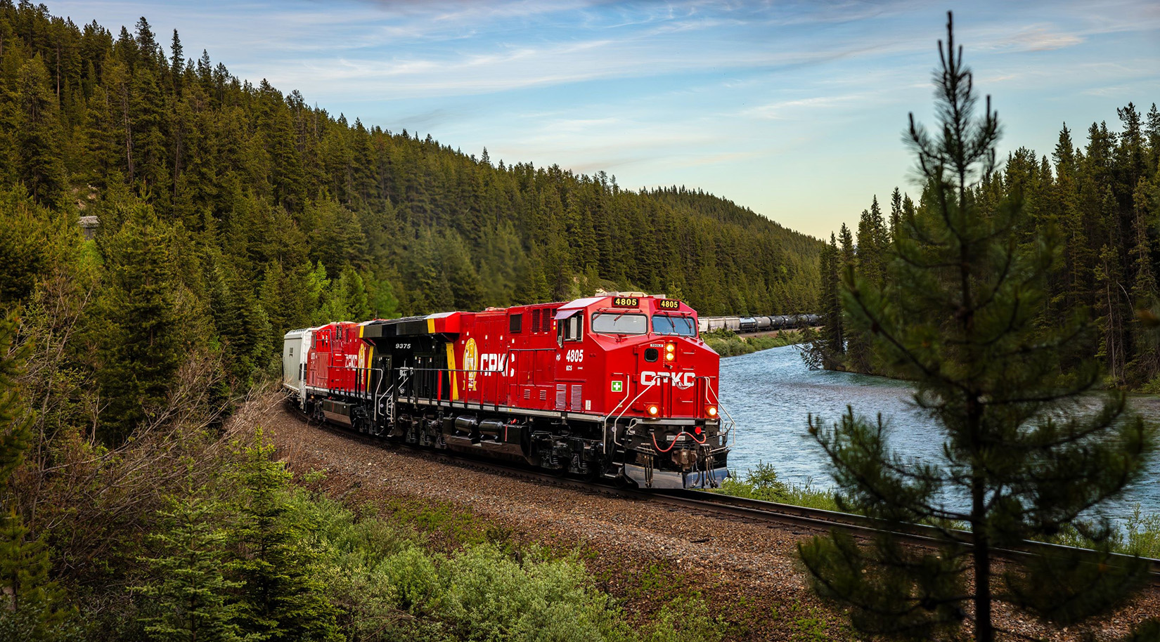 A red CPKC train engine crossing a bridge over water